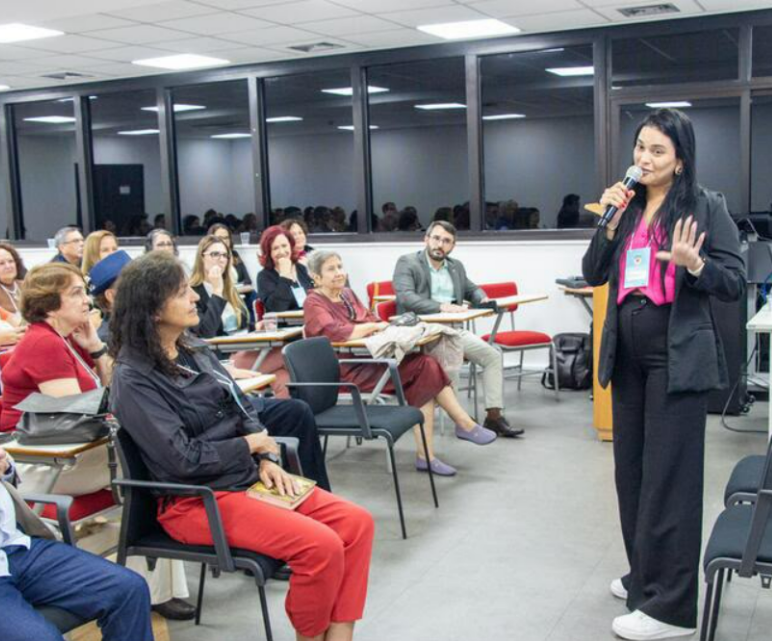 Lalesca palestrando com microfone para plateia em evento institucional